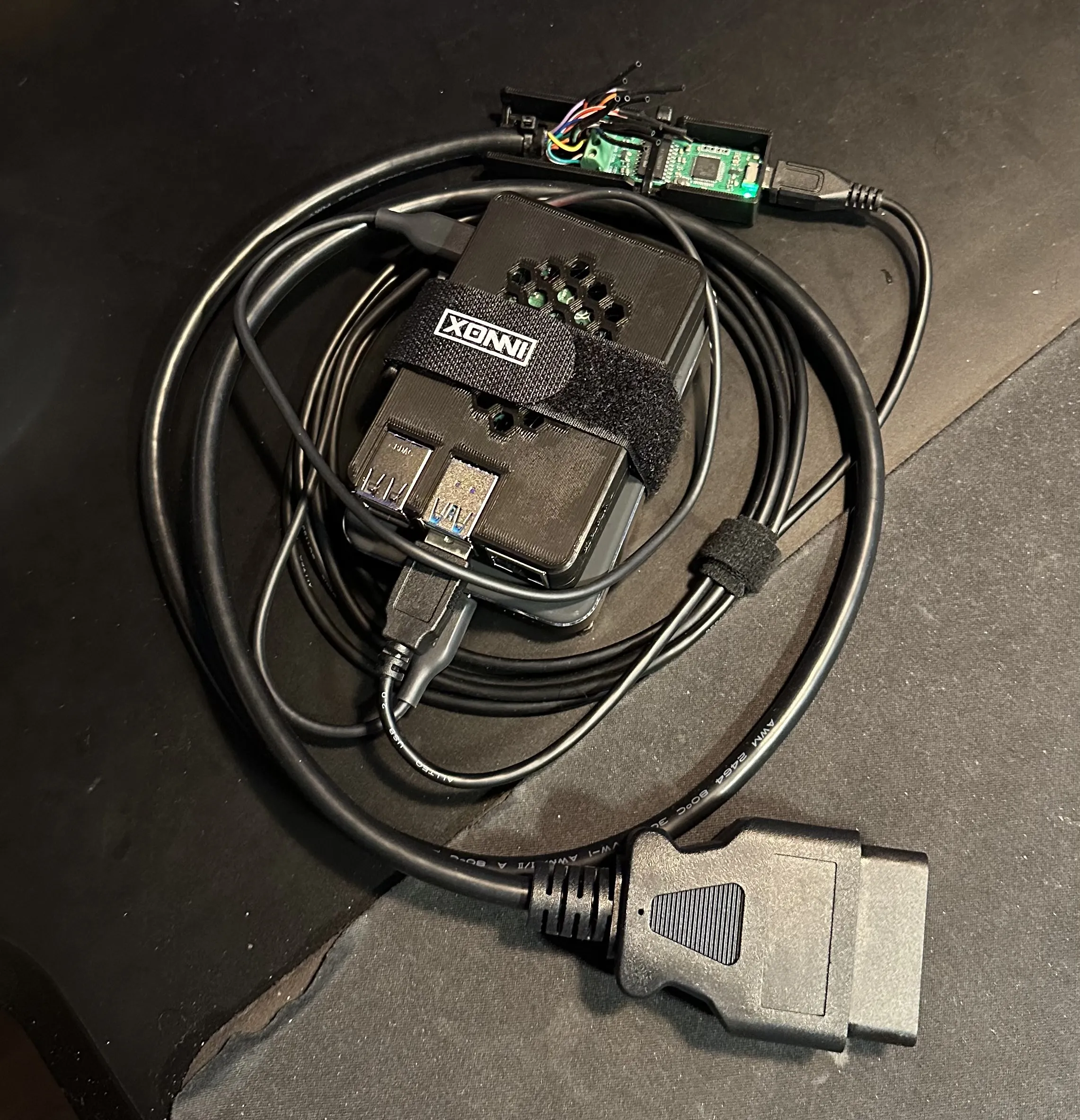 A Raspberry Pi 4 in a black case strapped to a power bank, wired to a CANable Pro USB-to-CAN adapter and an OBD-II pigtail cable
